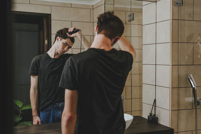 Young man with electric razor cutting his hair in bathroom