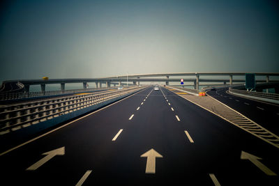 Road leading towards bridge against clear sky