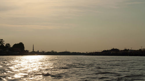 Silhouette buildings by sea against sky during sunset