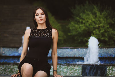 Portrait of young woman sitting against fountain