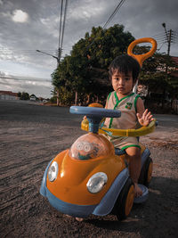 Portrait of cute boy on toy car against sky