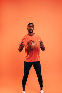 Portrait of man with basketball standing against orange background