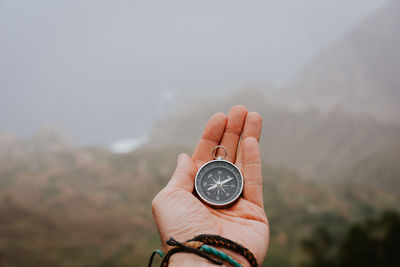 Cropped hand holding navigational compass against mountain