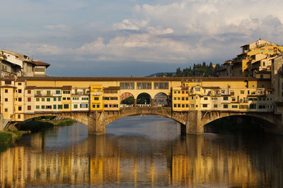 Arch bridge over river by buildings against sky in city