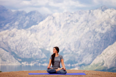 Young woman sitting by lake against mountains