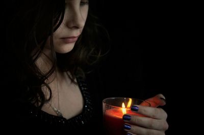 Close-up of young woman with lit tea light candle against black background