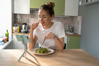 Woman vlogging while holding salad on table at home