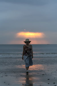 Rear view of woman standing at beach during sunset