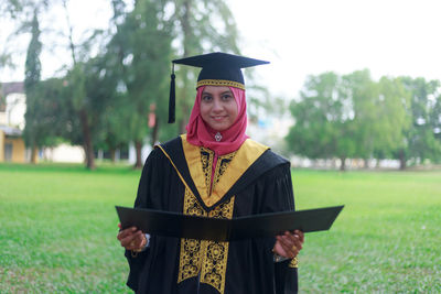 Portrait of woman in graduation gown standing on field