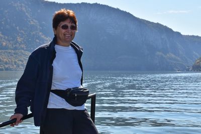 Portrait of woman smiling while standing at lakeshore against mountains