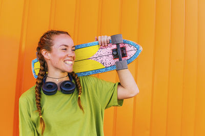 Portrait of a smiling young woman standing against yellow wall