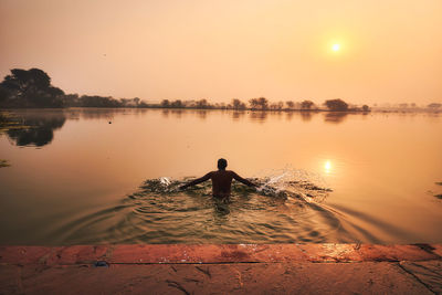 Rear view of man swimming in lake against clear sky during sunset