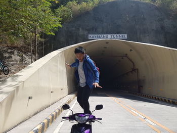 Full length of man balancing on scooter against tunnel by trees