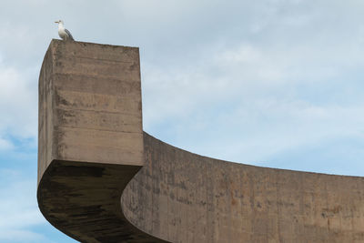 Seagull perched on a concrete structure against cloudy sky