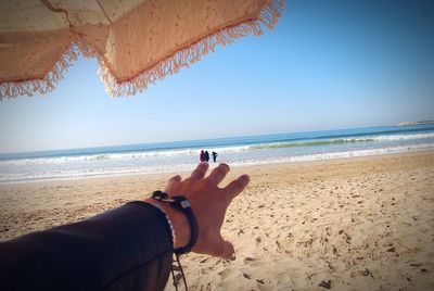 Midsection of hands on beach against sky