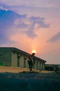 Surface level image of young man digging on field against sky during sunset