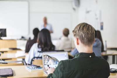 Cropped image of male student using laptop at desk in classroom