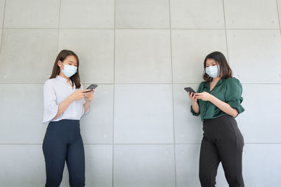 Full length of young woman using mobile phone against wall