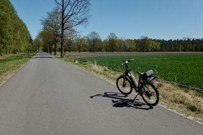 Bicycle on road amidst field against sky