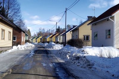 Snow covered houses by road against sky