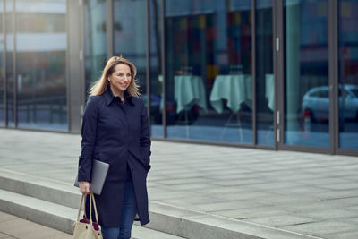 Smiling businesswoman standing by office building in city
