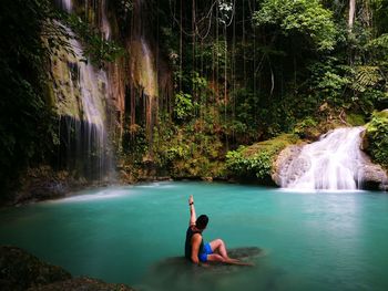 Young woman sitting on rock by waterfall