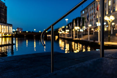 Illuminated buildings by river against sky at dusk