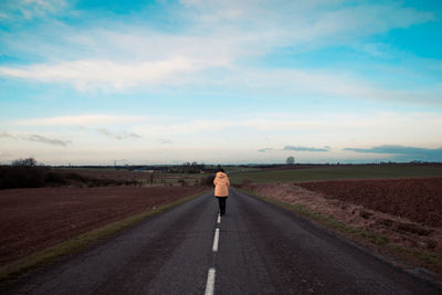 Rear view of woman walking on country road against sky