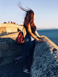 Woman with arms raised against sea against sky