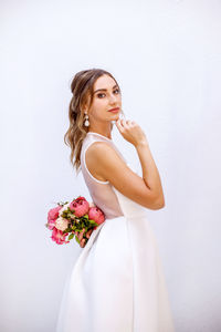 Young woman standing by pink flower against white background
