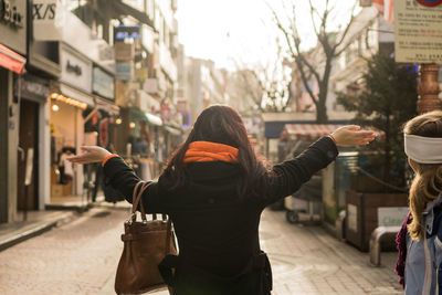 Rear view of woman with arms outstretched standing on street in city