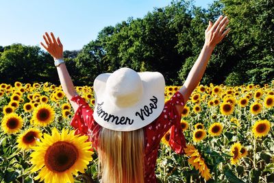 Rear view of woman with arms outstretched standing amidst sunflowers