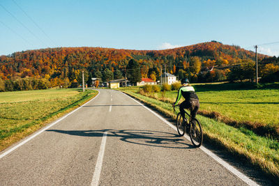 Rear view of woman riding bicycle on road against sky