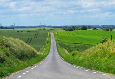 Panoramic view of road amidst field against sky