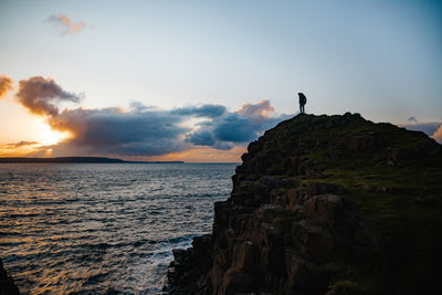 People looking at sea shore against sky during sunset