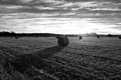 Hay bales on field against cloudy sky