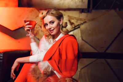 Portrait of young woman holding cocktail while sitting in nightclub