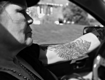 Close-up of mature woman with tattoo driving car on sunny day