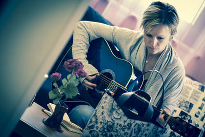 Woman with short hair playing guitar at home