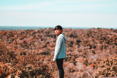 Side view portrait of young man standing on land against sky during sunny day