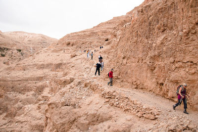 People walking on rock formations against sky