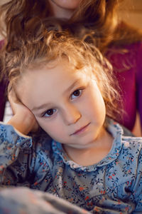 Mother in purple clothes with a sad dissatisfied daughter in a dress is sitting on a bed in a hotel