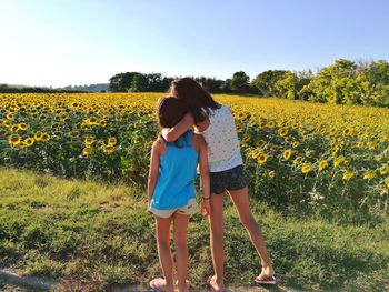 Rear view of siblings standing by sunflowers on farm