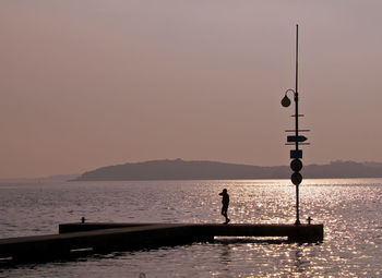 Silhouette people fishing in sea against sky during sunset