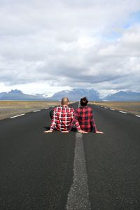 Rear view of couple sitting on road against mountains