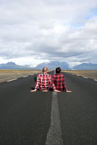 Rear view of men sitting on road against sky