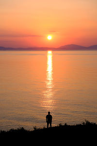 Silhouette woman walking at beach against sky during sunset