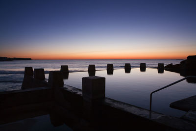 Wooden posts in sea against clear sky during sunset