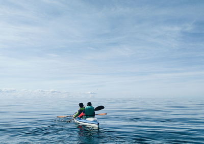 Rear view of friends kayaking on sea against sky
