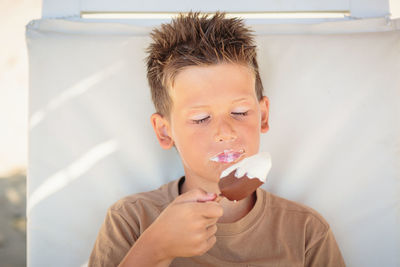 Handsome boy sitting on the beach and eating ice cream